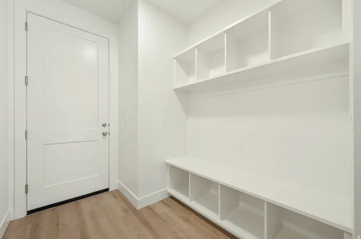Entryway featuring built-in white cabinetry with open shelving, a white paneled door with brushed nickel hardware, and wood-finish flooring