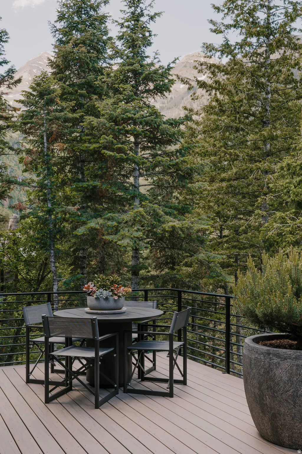 Expansive outdoor deck featuring composite decking, a black metal horizontal railing, and a mountainous backdrop with abundant evergreen trees