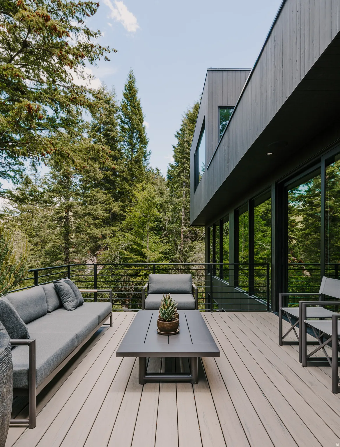 Expansive outdoor deck featuring wood-finish decking, a black metal railing, and extensive surrounding mature trees