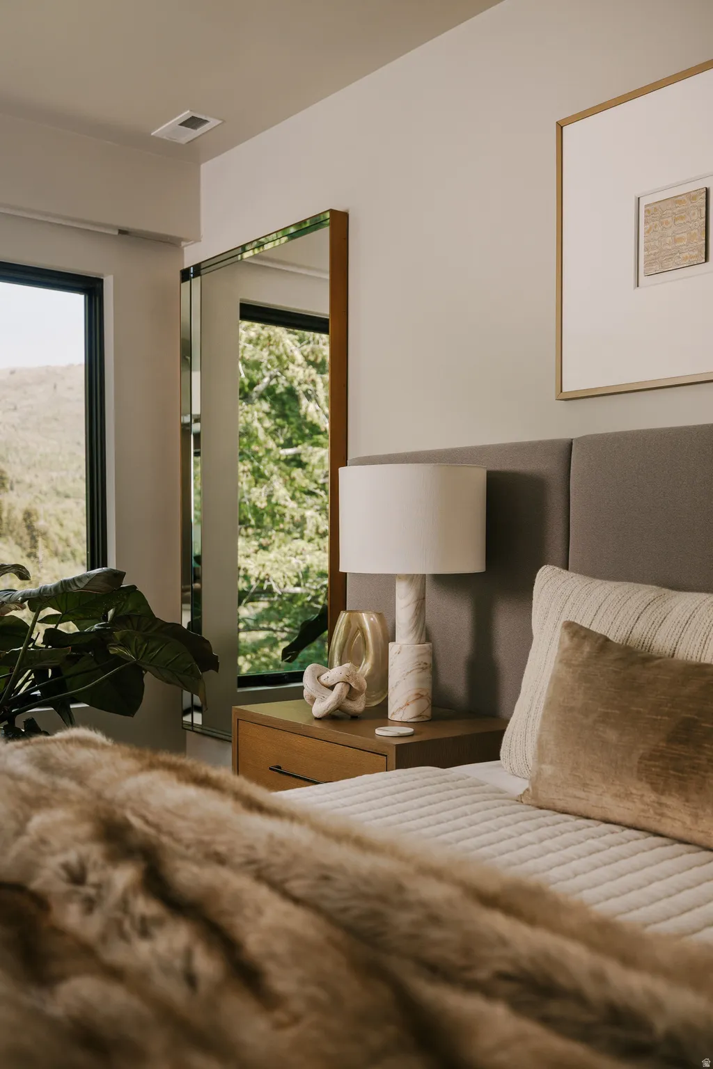 Bedroom featuring an upholstered headboard, a wood-finish nightstand, a built-in mirror, and expansive windows