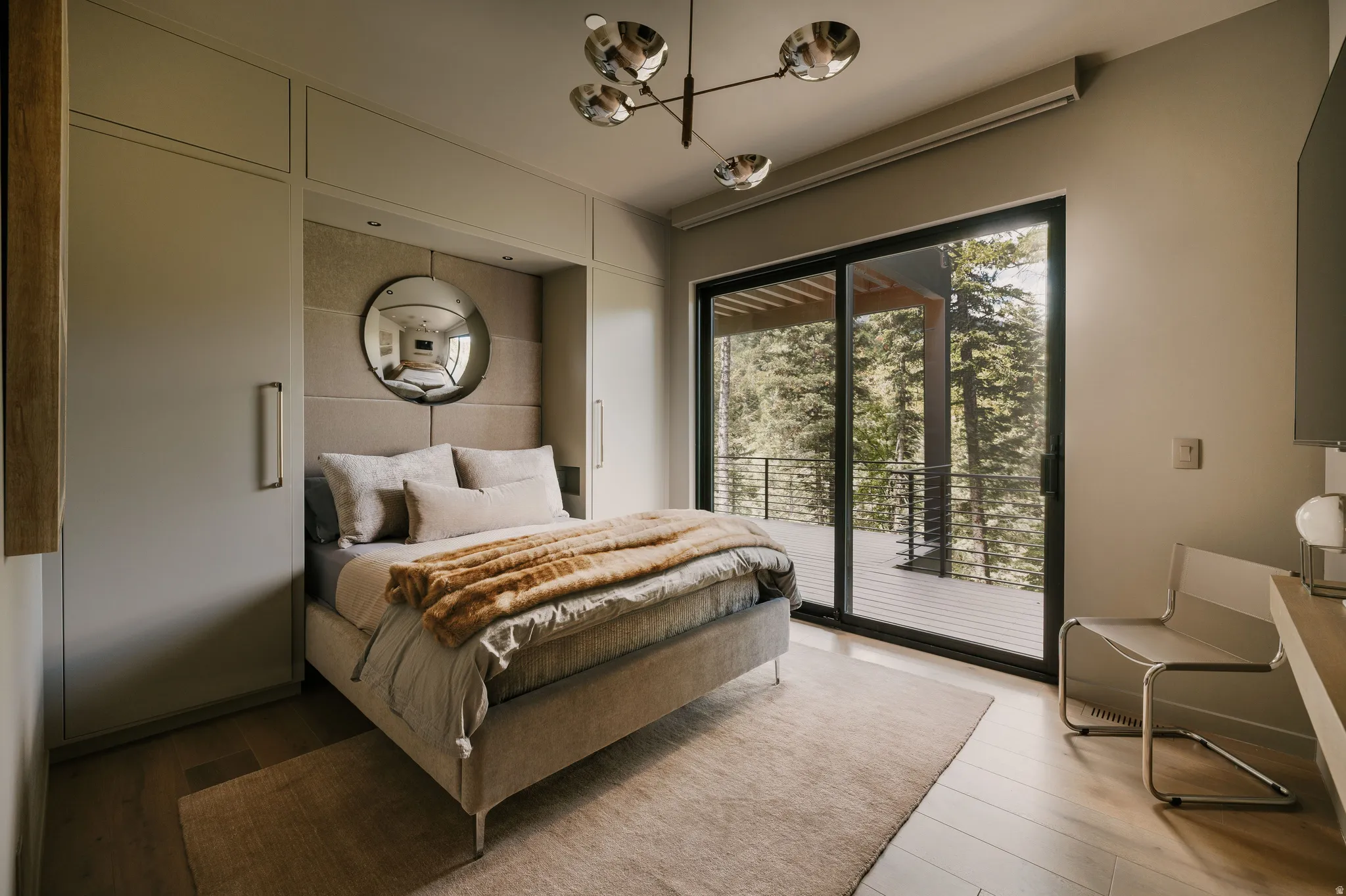 Floor-to-ceiling sliding glass doors open to a private balcony overlooking a wooded landscape