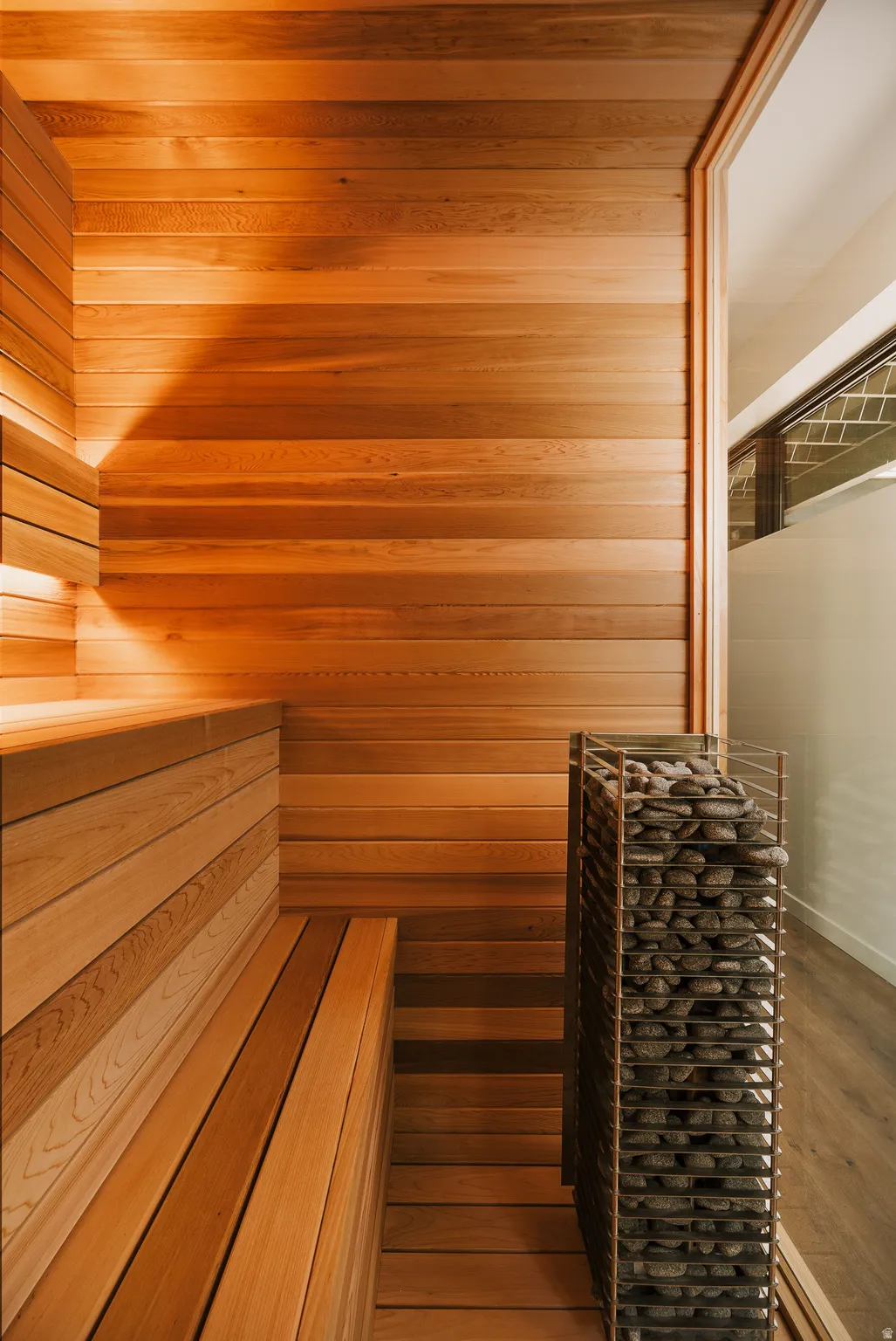 Dedicated sauna featuring horizontal wood-finish paneling, built-in wooden bench seating, and a stone-filled heating unit