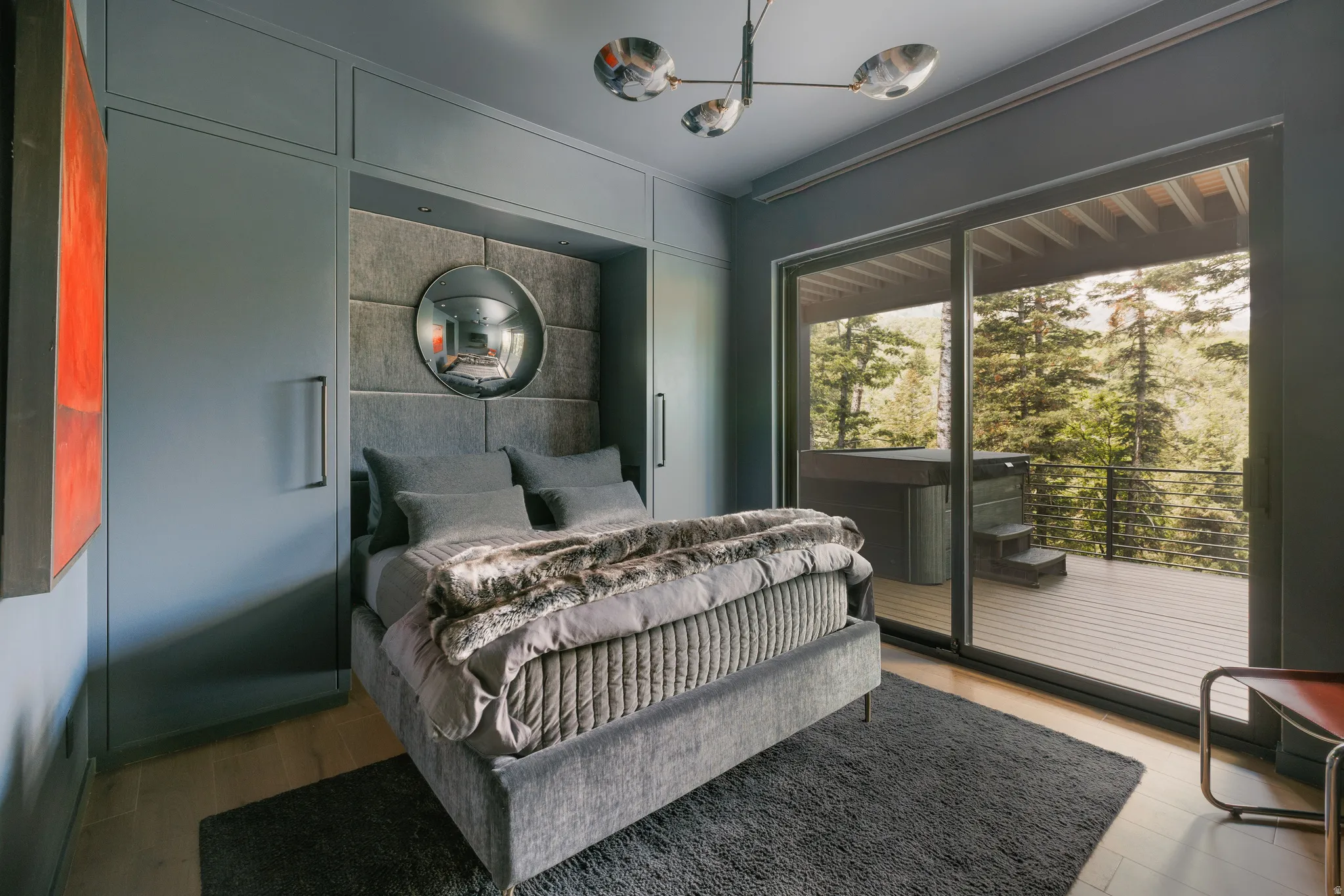 Bedroom featuring built-in cabinetry, wood-finish flooring, a contemporary chandelier, and a sliding glass door opening to an outdoor deck