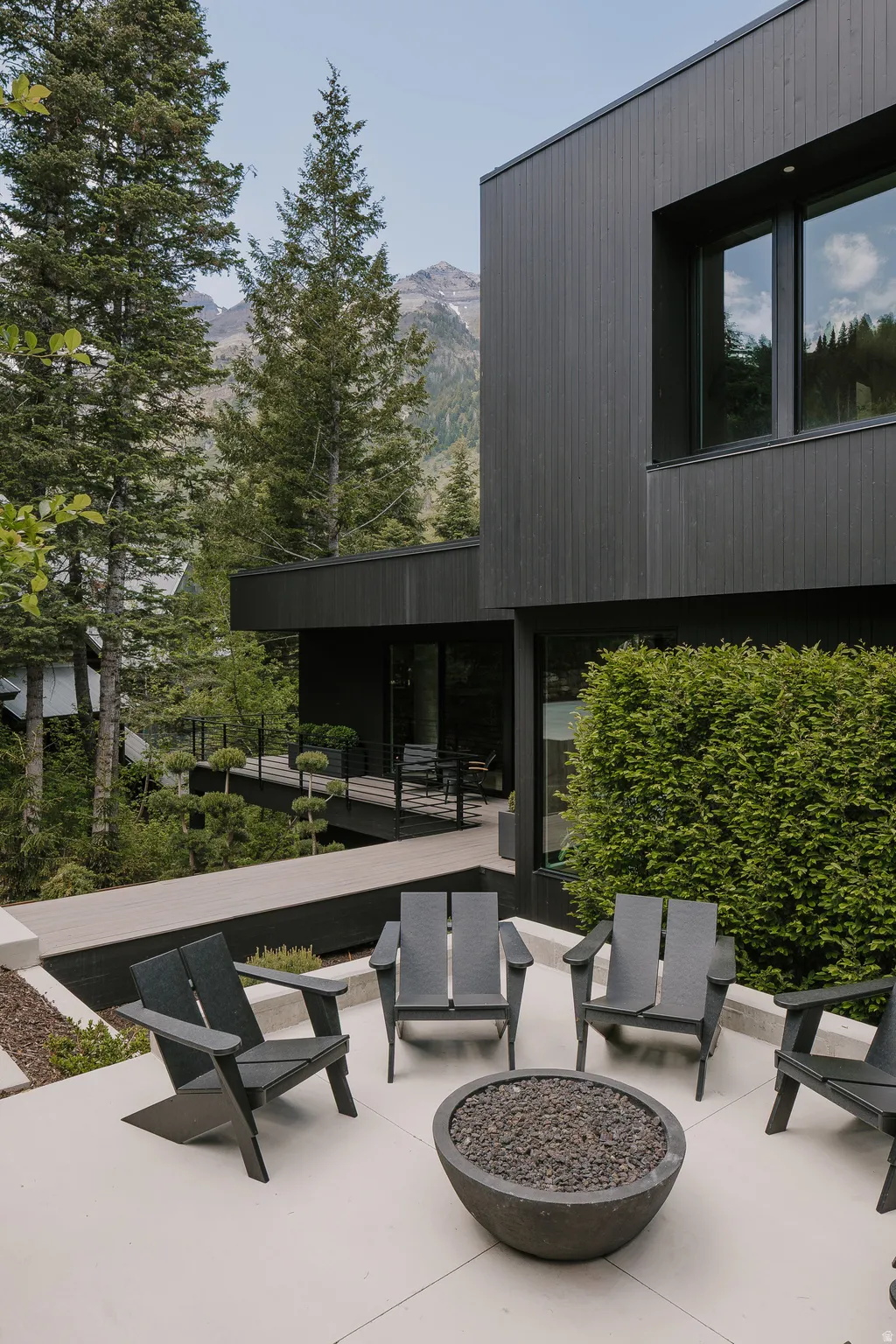 Outdoor patio featuring a concrete fire pit, four Adirondack-style chairs, and a contemporary dark-paneled exterior