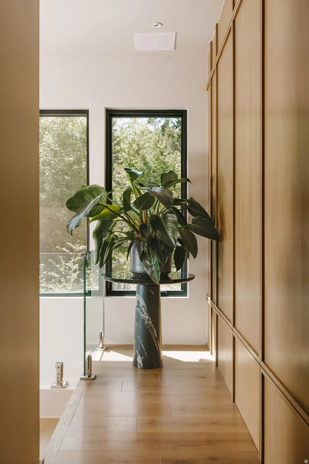 Hallway with wood-finish flooring, full-height paneled walls, and a glass railing system