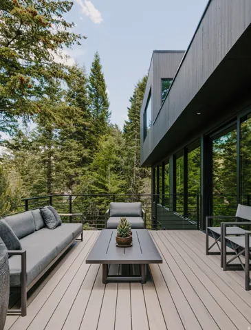 Expansive outdoor deck featuring wood-finish decking, a black metal railing, and extensive surrounding mature trees