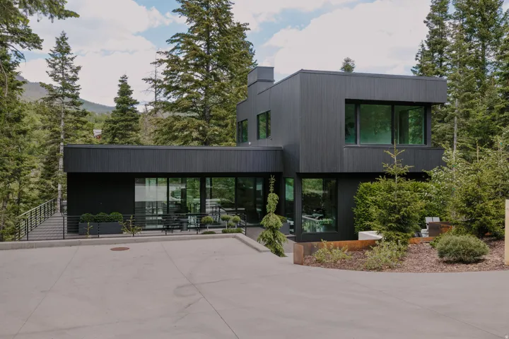 Modern black exterior with expansive windows, concrete driveway, and mature landscaping