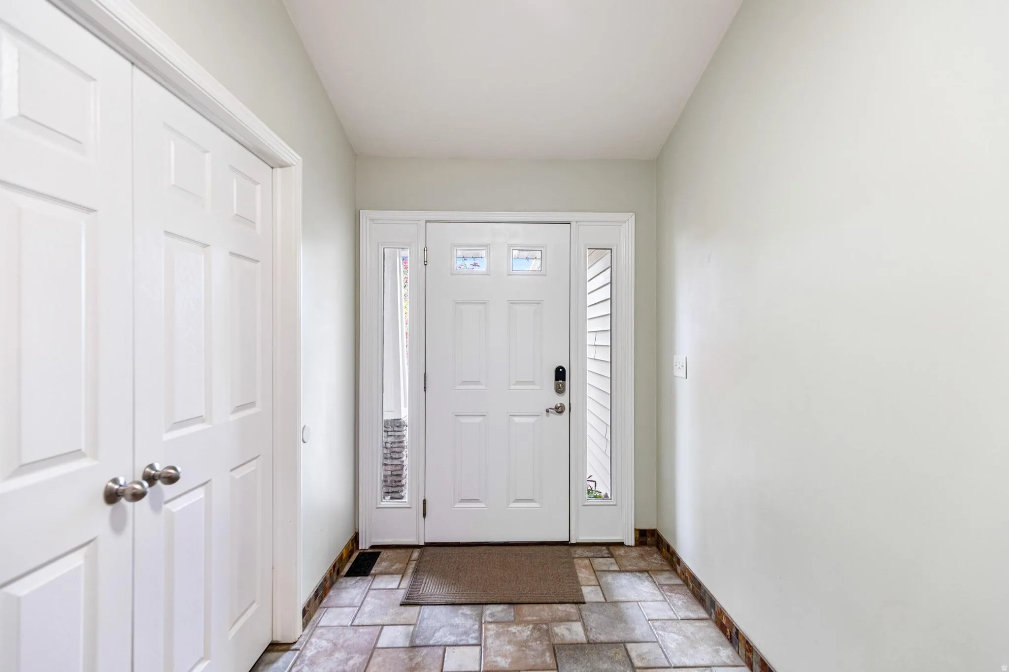 Extra wide entryway featuring a white paneled door with decorative glass inserts, sidelight windows, and a multi-tone tile floor