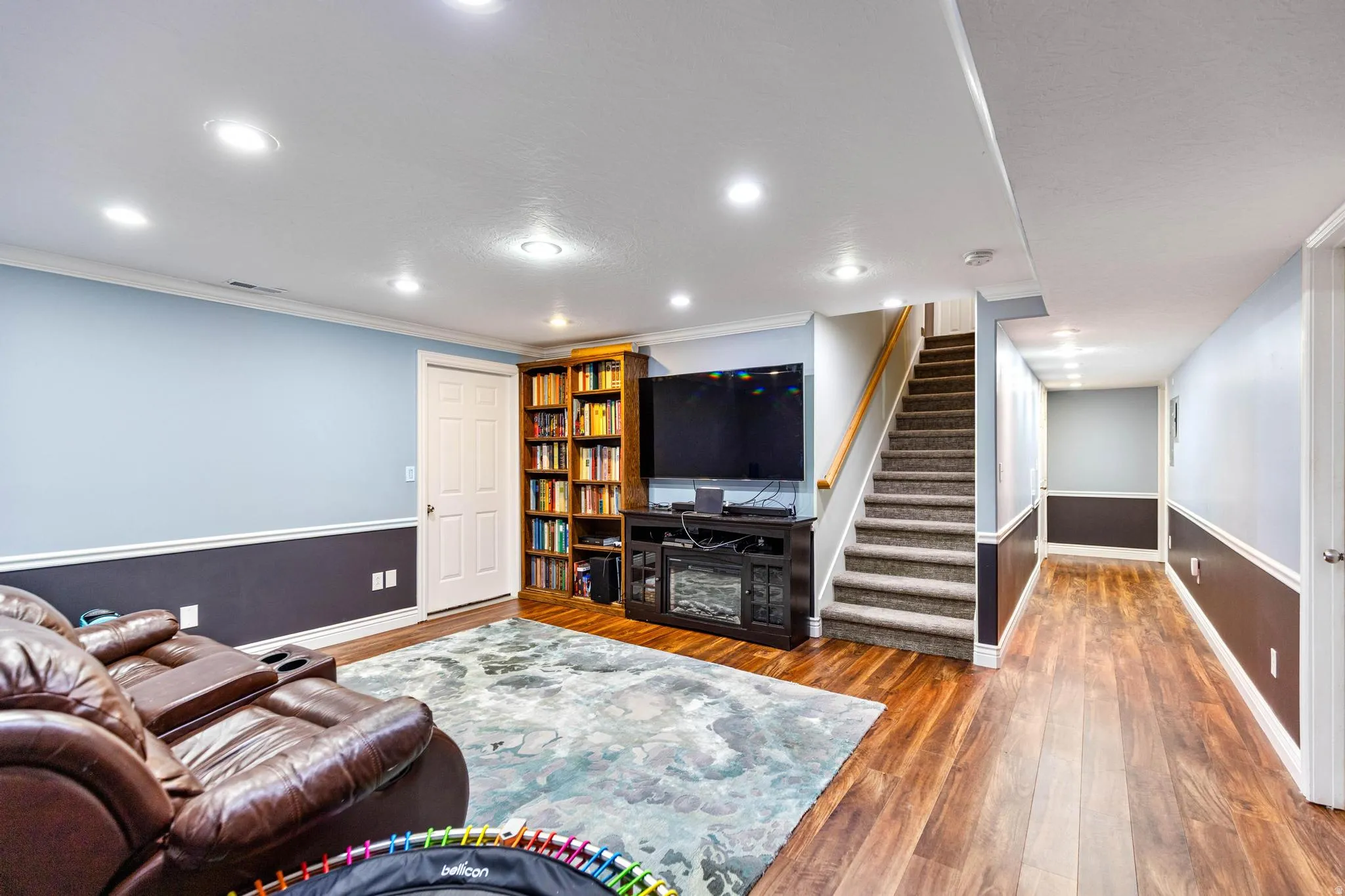 Finished lower level featuring recessed lighting, two-tone wall treatment, wood-finish flooring, a built-in entertainment center, and a carpeted staircase with wood railing