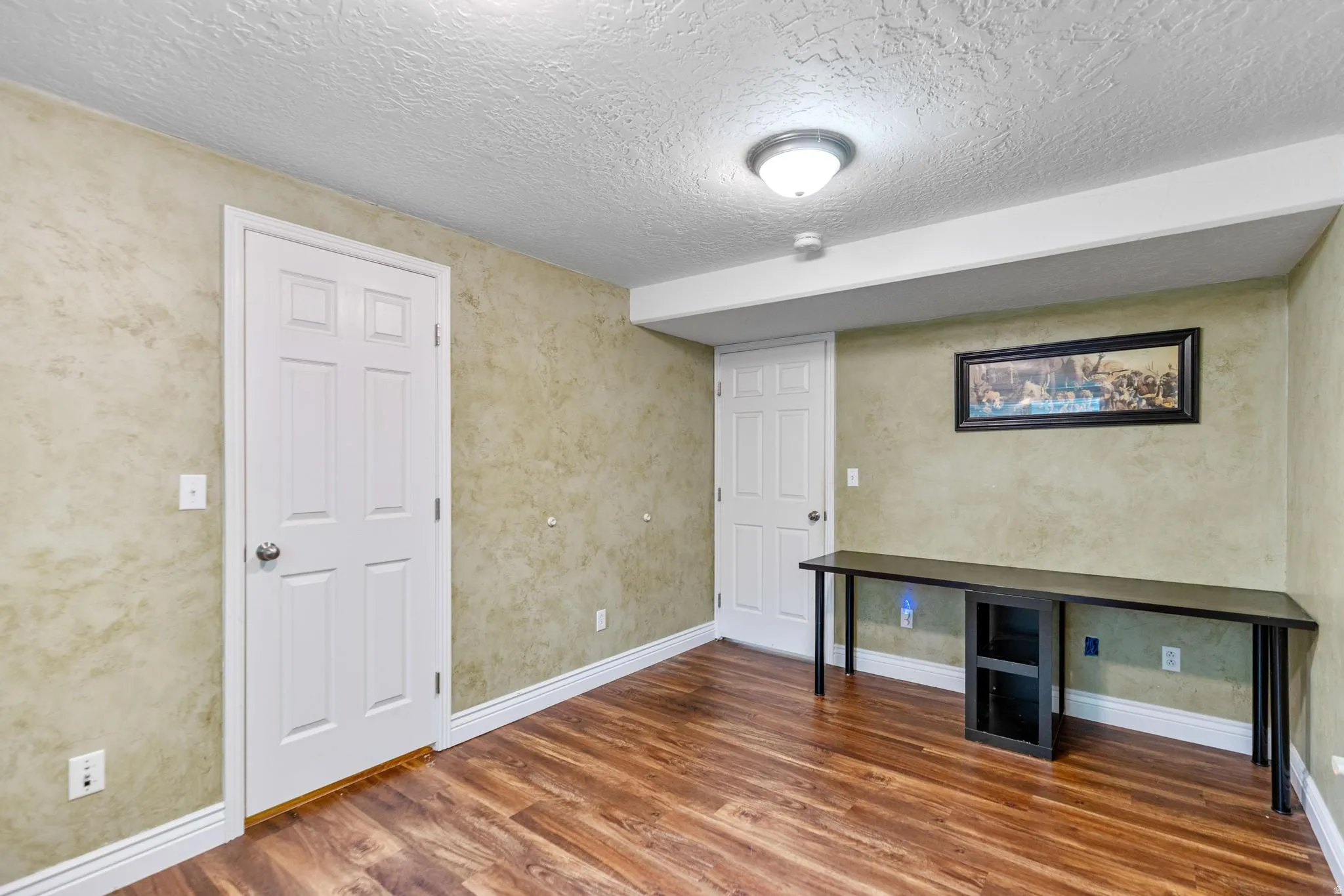 Room featuring wood-finish flooring, textured walls, and a built-in wall-length desk with integrated shelving