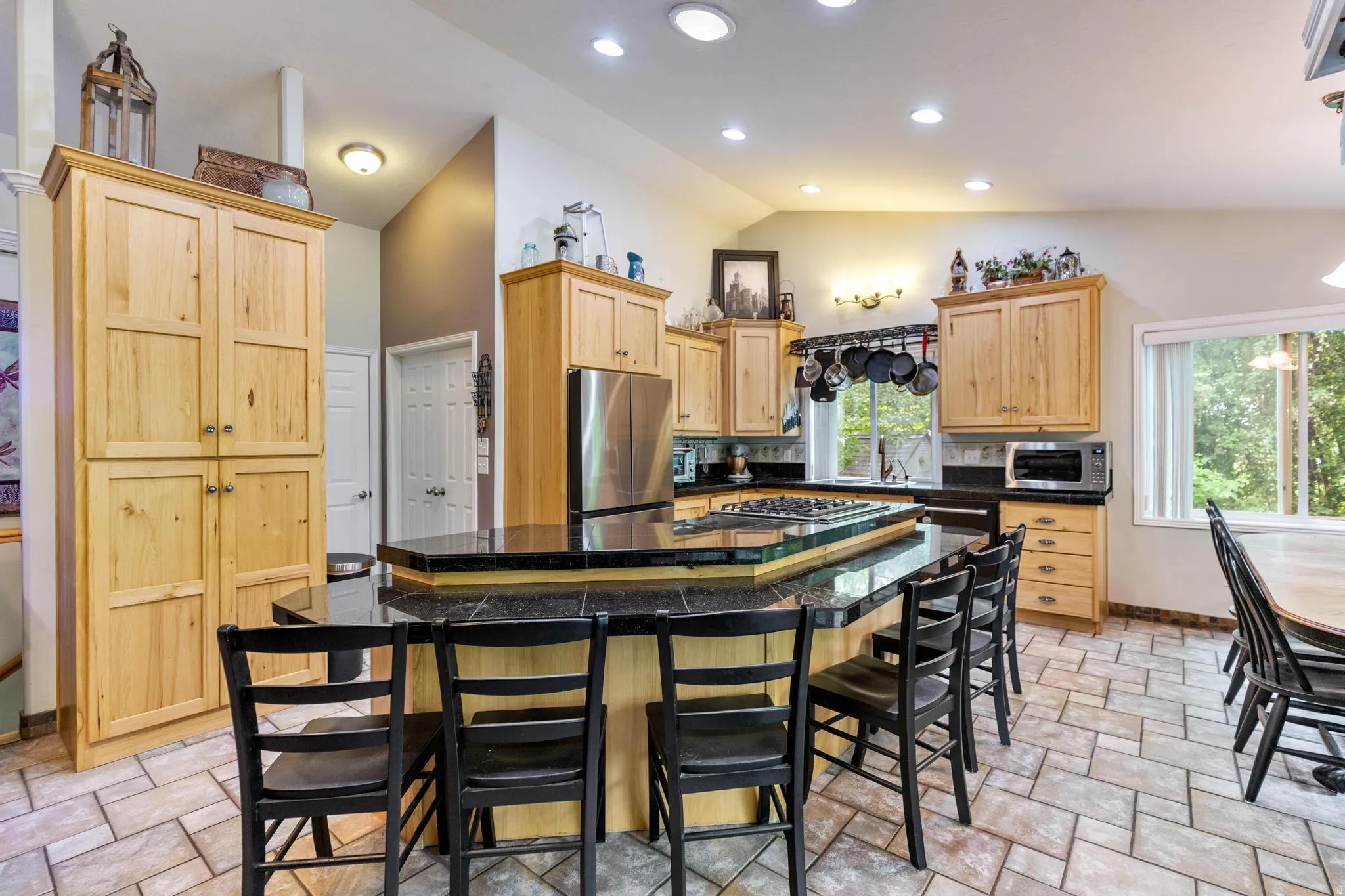 Spacious kitchen featuring an angular breakfast bar with built-in cooktop, light wood cabinetry, recessed lighting, and tile flooring