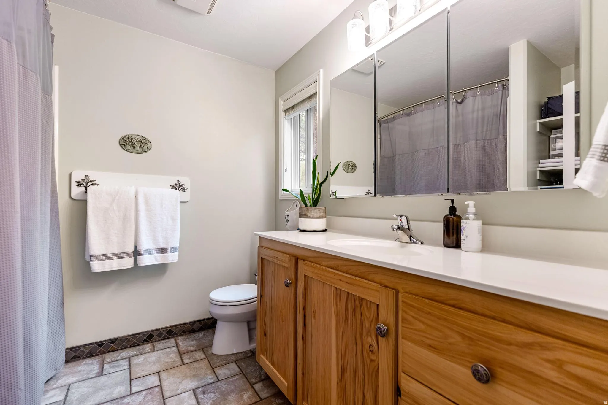 Bathroom featuring a light wood-finish vanity with a white countertop and integrated sink, chrome faucet, and three mirrored medicine cabinets
