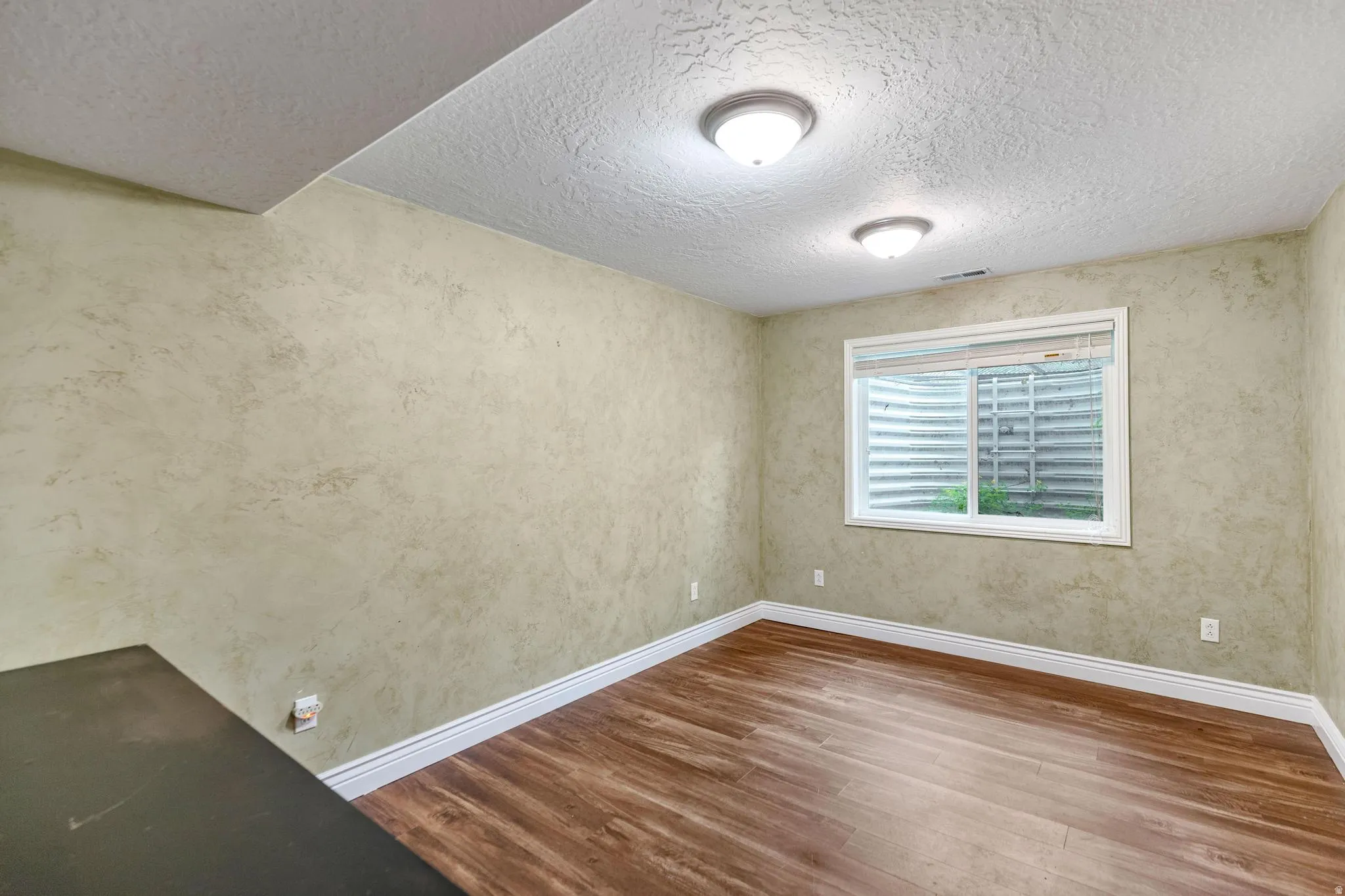 Room featuring wood-finish flooring, textured walls, and a window with blinds