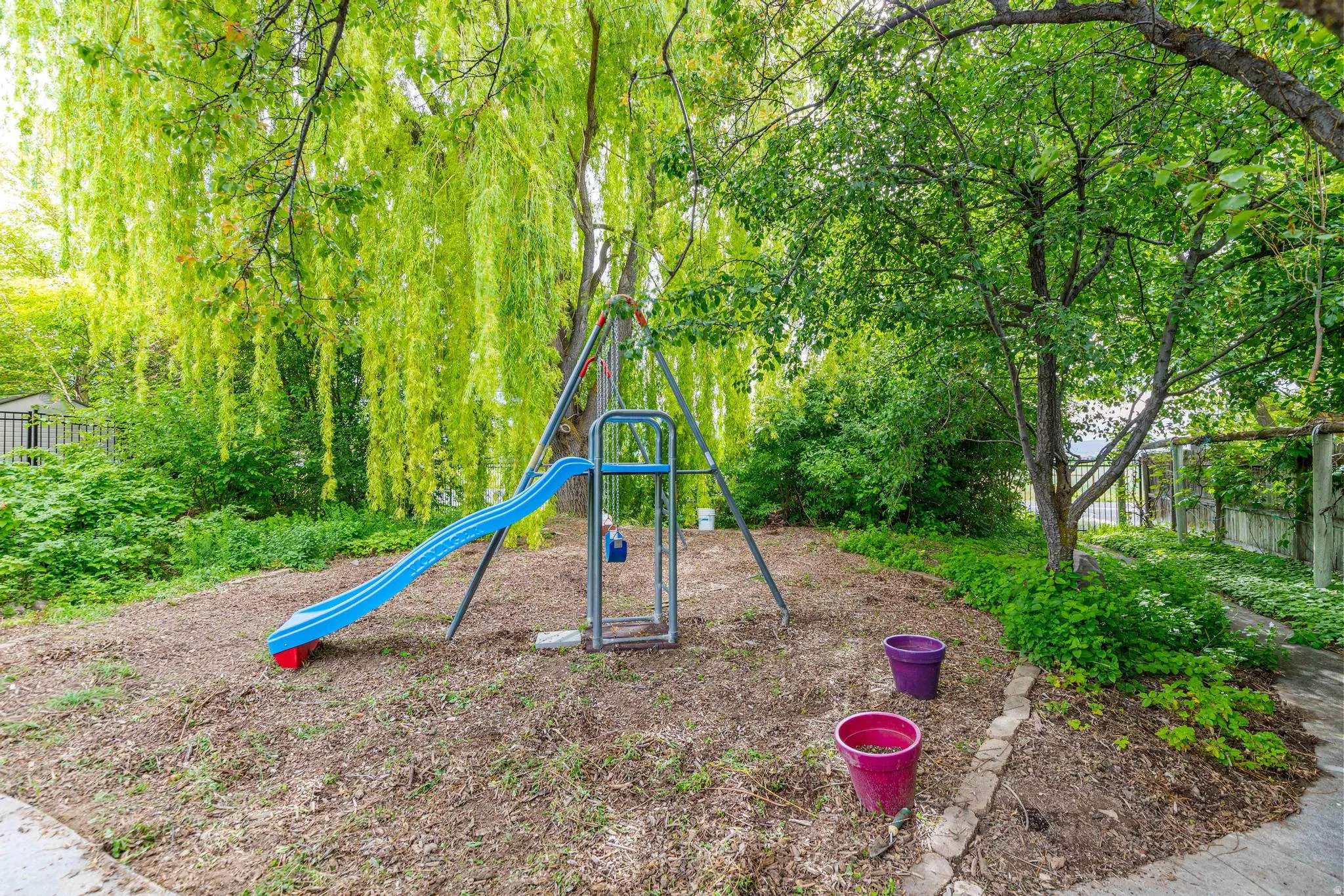 Generous outdoor space featuring mature trees and a swing set with a slide