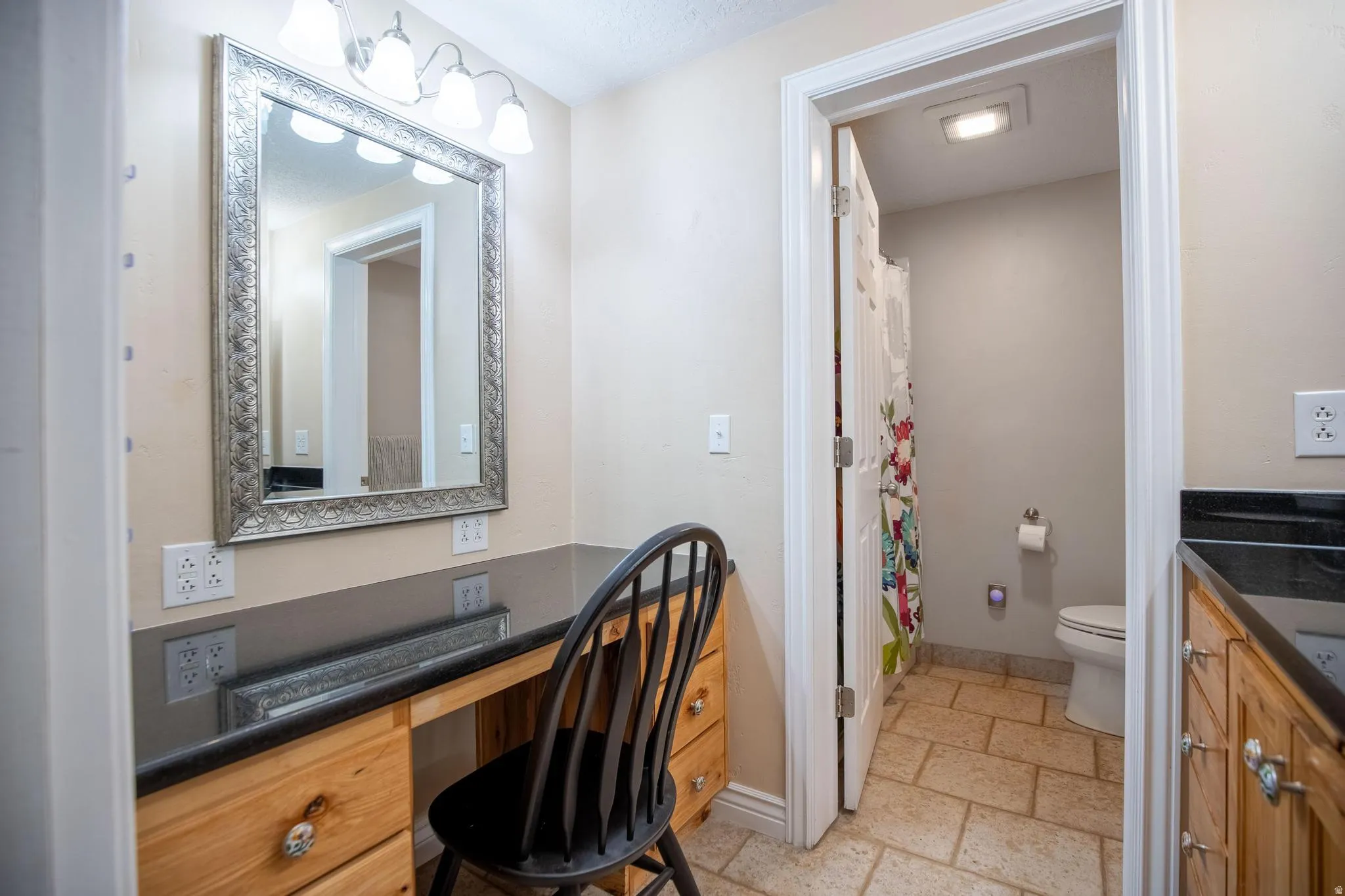 Vanity area featuring a large framed mirror, four-light fixture, wood-finish cabinetry, and dark countertop