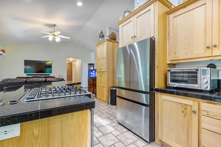 Kitchen island with a free standing gas cooktop, down vent, tile countertops, natural wood cabinetry, and stainless steel appliances