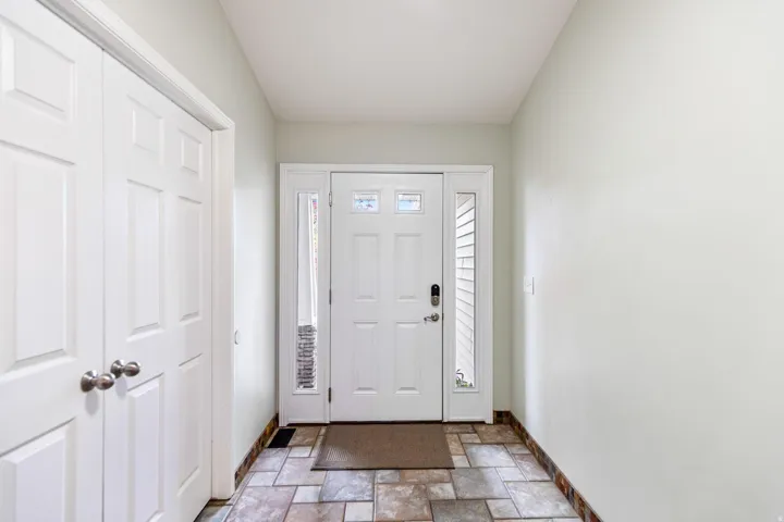 Extra wide entryway featuring a white paneled door with decorative glass inserts, sidelight windows, and a multi-tone tile floor