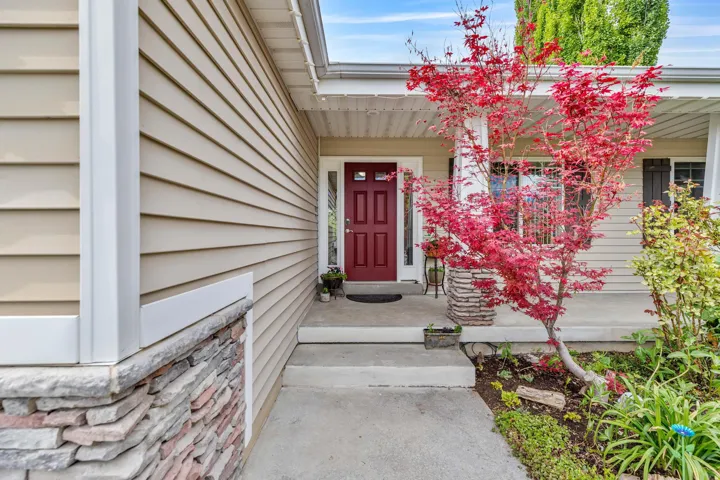 Inviting entry featuring a red paneled door, stone-clad columns, and open wide front porch looking out over immaculate landscaping
