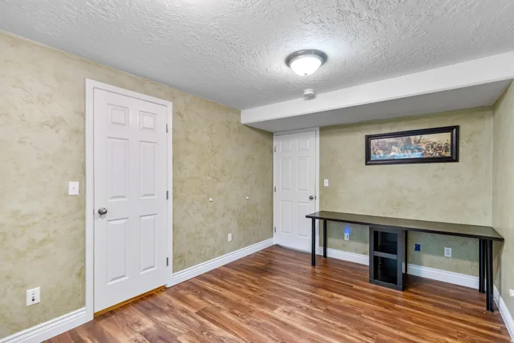 Room featuring wood-finish flooring, textured walls, and a built-in wall-length desk with integrated shelving