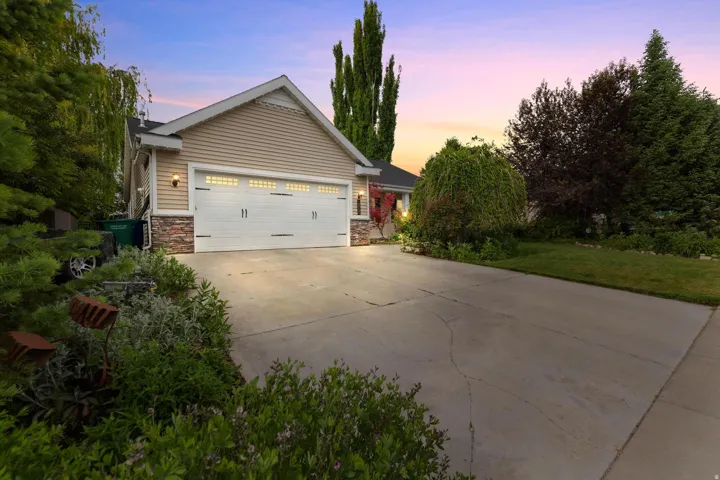 Exterior featuring horizontal siding, stone facade accents, a two-car garage with panel doors and decorative windows, a concrete driveway, and mature landscaping