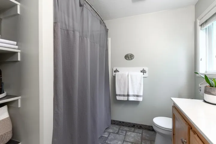 Bathroom featuring a shower with a curved curtain rod, light wood-finish vanity with a light countertop, built-in shelving, tiled flooring, and a window for natural light