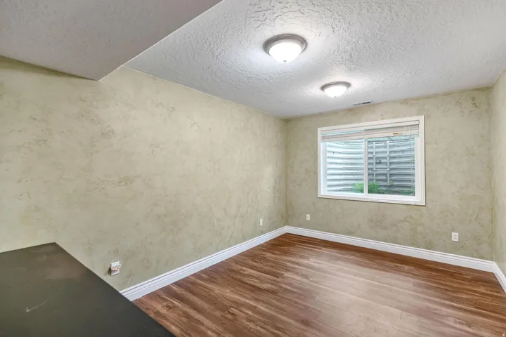 Room featuring wood-finish flooring, textured walls, and a window with blinds