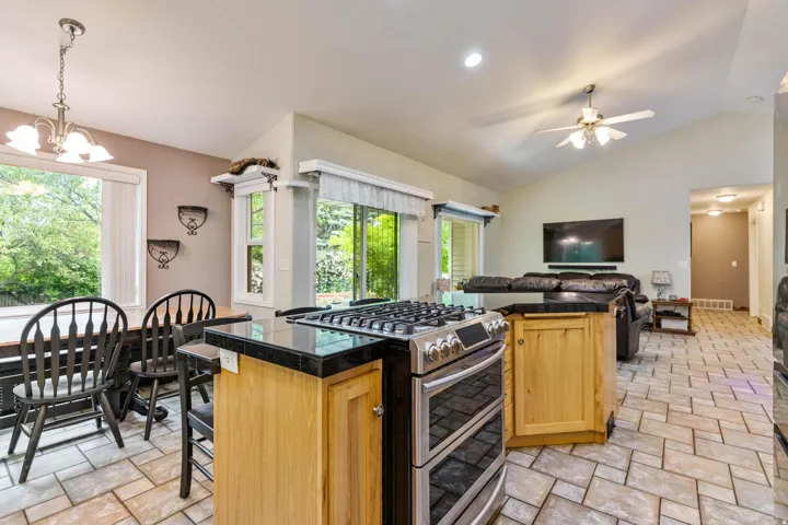 Kitchen island with black countertop and gas range (can be either gas or electric), open to a living area with vaulted ceilings and a ceiling fan