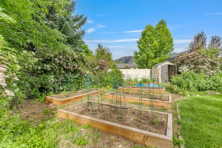 Backyard garden featuring four raised planting beds, a white vinyl privacy fence, and a storage shed