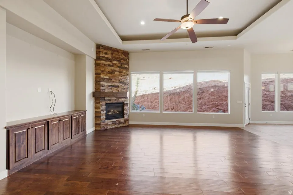 Spacious room featuring wood-finish flooring, a stacked stone fireplace with a wood mantle, and multiple large windows