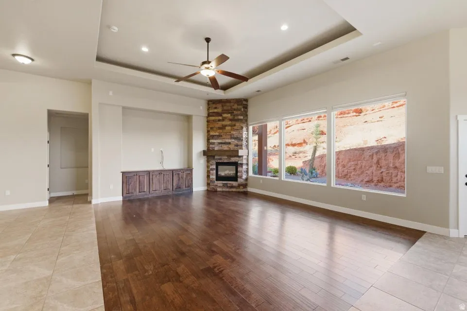 Spacious room featuring multiple large windows, a corner stone fireplace with a wood mantle, an integrated entertainment console with dark wood cabinetry, a ceiling fan, and recessed lighting