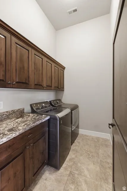 Laundry area featuring dark wood-finish cabinetry with silver hardware, a granite-finish countertop, and tile flooring