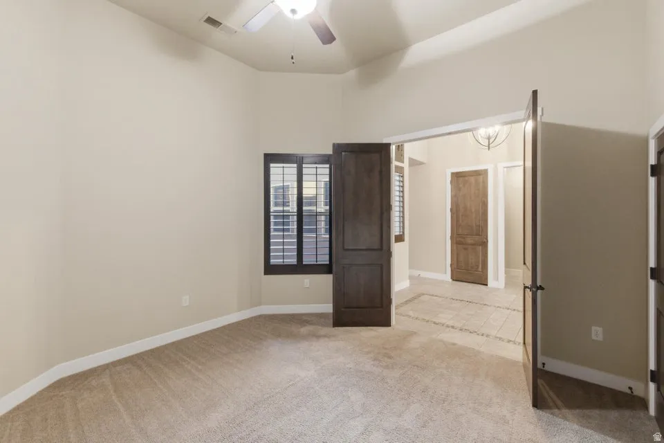 Carpeted room featuring a ceiling fan, vaulted ceiling, plantation shutters, and double doors