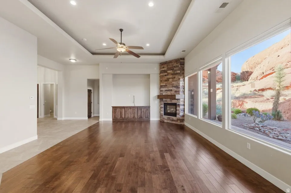 Spacious living area featuring wood-finish flooring, a stone-clad fireplace with a wood mantle, and a built-in entertainment center with wood cabinetry