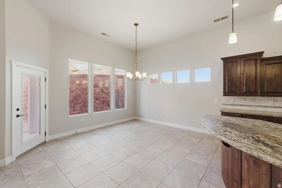 Spacious dining area featuring vaulted ceilings, light tile flooring, a contemporary chandelier, large windows, and a built-in kitchen peninsula with a stone countertop