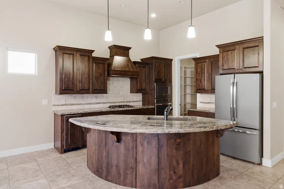 Gourmet kitchen featuring a curved island with stone countertop, stainless steel appliances, dark wood cabinetry, tile flooring, and pendulum lighting