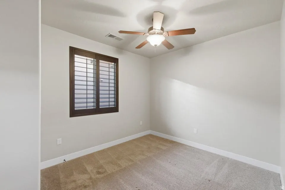 Bedroom featuring plantation shutters, neutral wall tones, a ceiling fan with light fixture, and carpet flooring