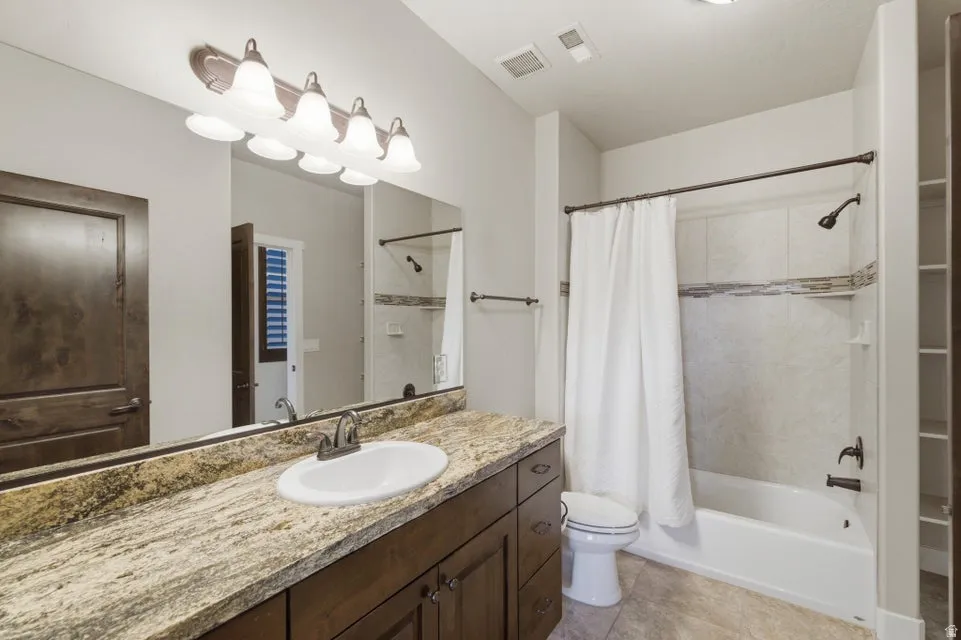 Bathroom featuring a spacious vanity with a granite-style countertop, undermount sink, and dark wood cabinetry