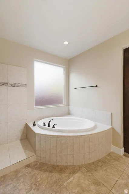 Built-in soaking tub with matte black fixtures, set within a tiled surround featuring a privacy window