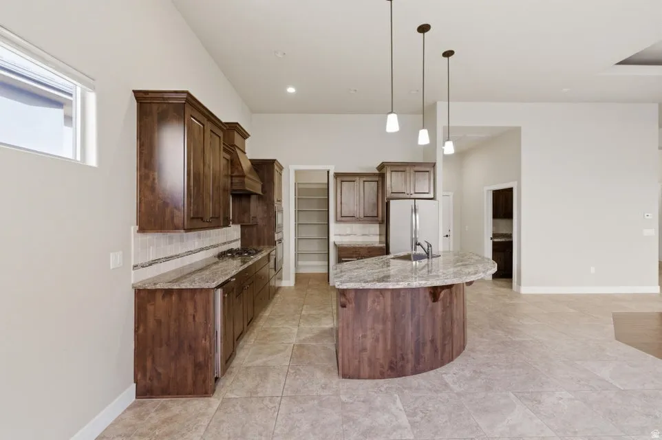 Modern kitchen featuring rich wood cabinetry, granite countertops, stainless steel appliances, and a curved island with pendant lighting
