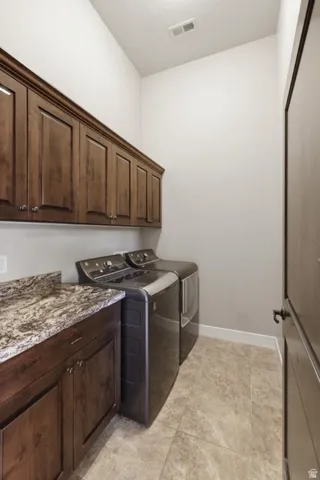Laundry area featuring dark wood-finish cabinetry with silver hardware, a granite-finish countertop, and tile flooring