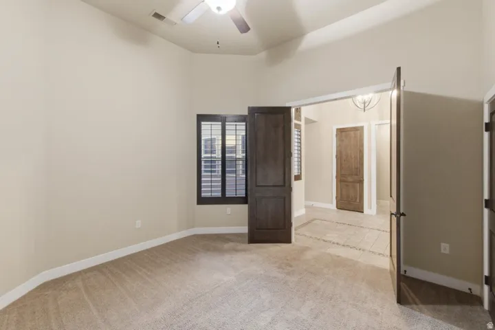 Carpeted room featuring a ceiling fan, vaulted ceiling, plantation shutters, and double doors