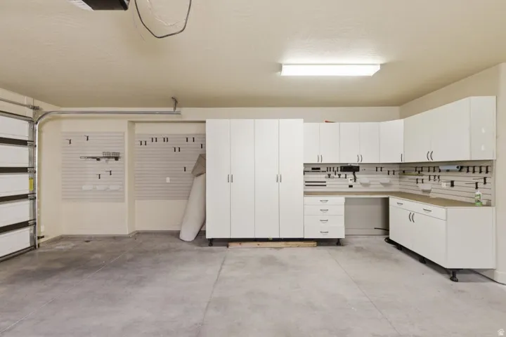 Garage space featuring integrated white cabinetry, durable concrete flooring, a corner workspace, overhead storage solutions, and slatwall organizational panels