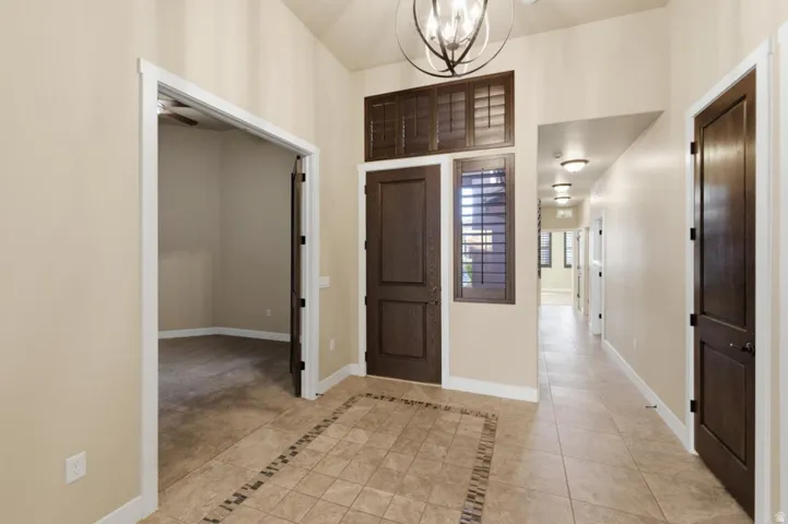 Entryway featuring ceramic tile flooring with decorative inlay, dark wood-finish doors, plantation shutters, and a vaulted ceiling with an overhead light fixture