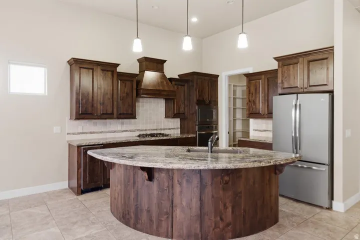 Gourmet kitchen featuring a curved island with stone countertop, stainless steel appliances, dark wood cabinetry, tile flooring, and pendulum lighting