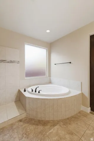 Built-in soaking tub with matte black fixtures, set within a tiled surround featuring a privacy window