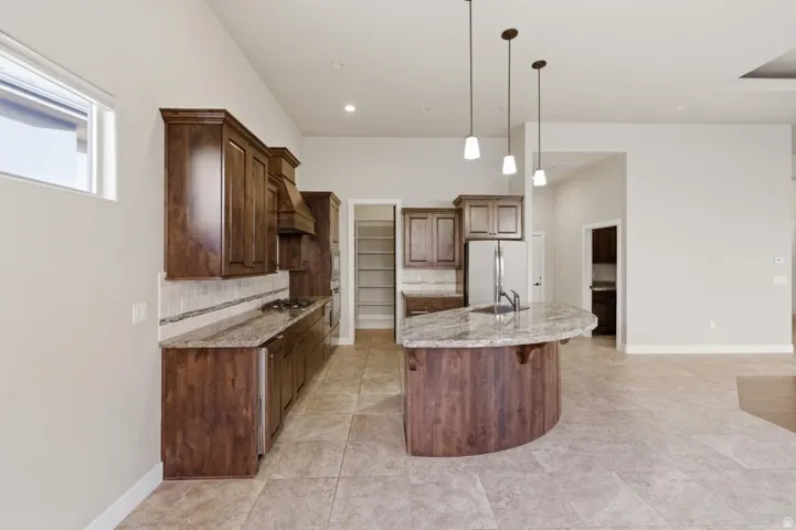 Modern kitchen featuring rich wood cabinetry, granite countertops, stainless steel appliances, and a curved island with pendant lighting