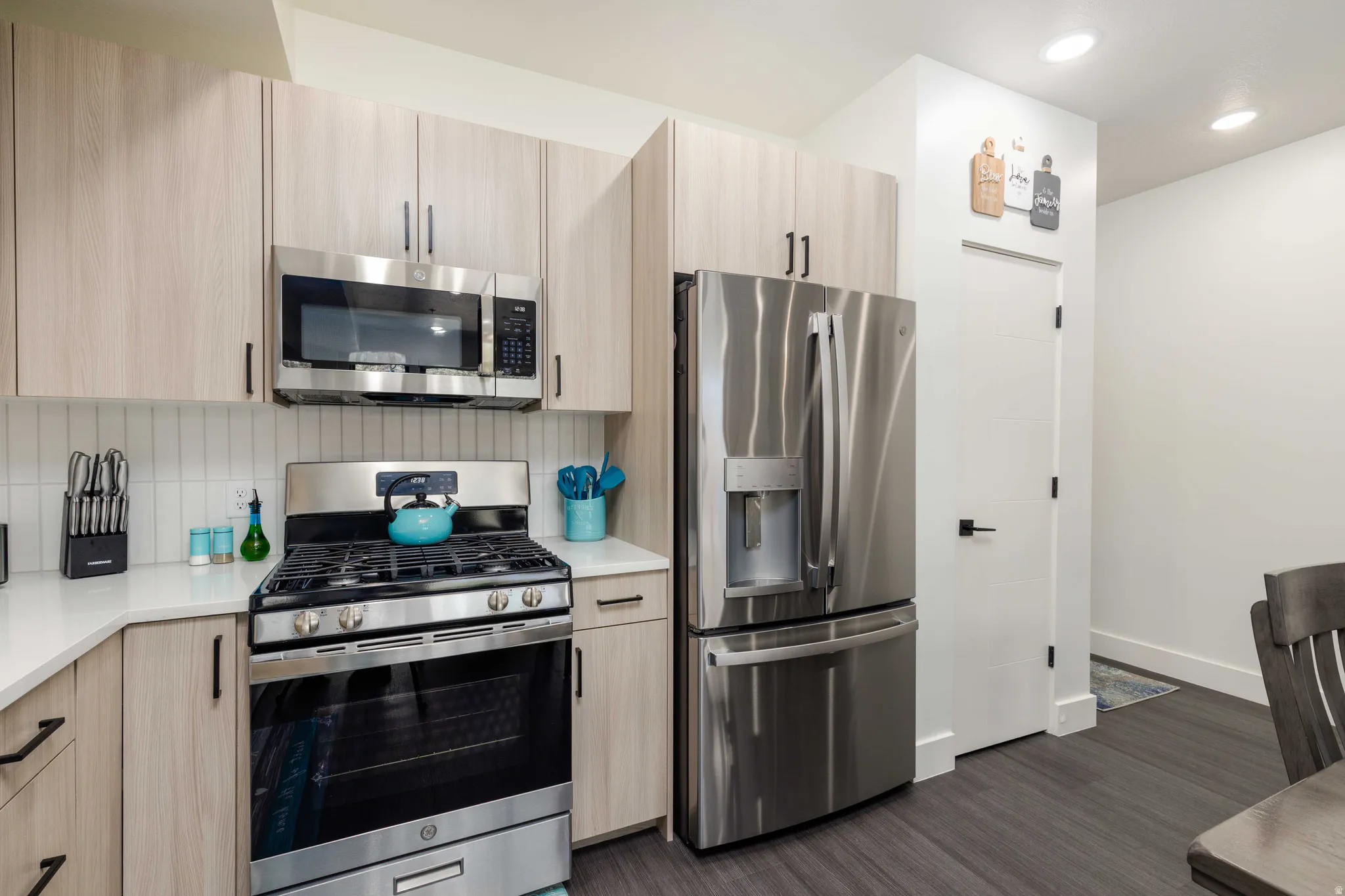 Modern kitchen featuring stainless steel appliances, light wood-finish cabinetry, a white subway tile backsplash, and dark wood-finish flooring