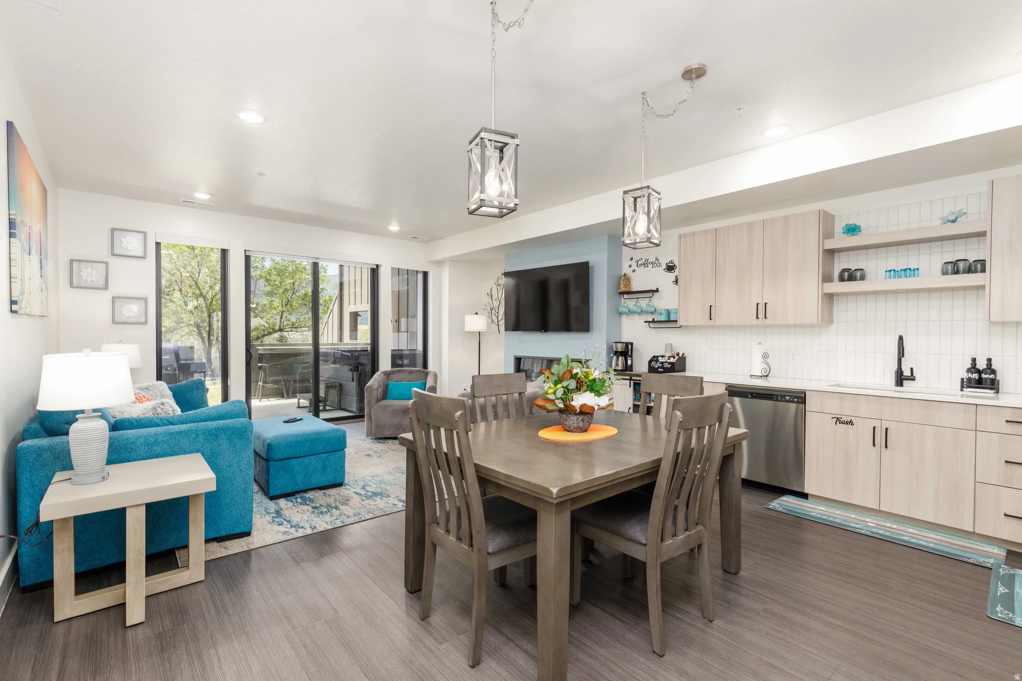 Open-concept living area featuring wood-finish flooring, a contemporary kitchen with light wood-finish cabinetry, stainless steel appliances, and a tiled backsplash