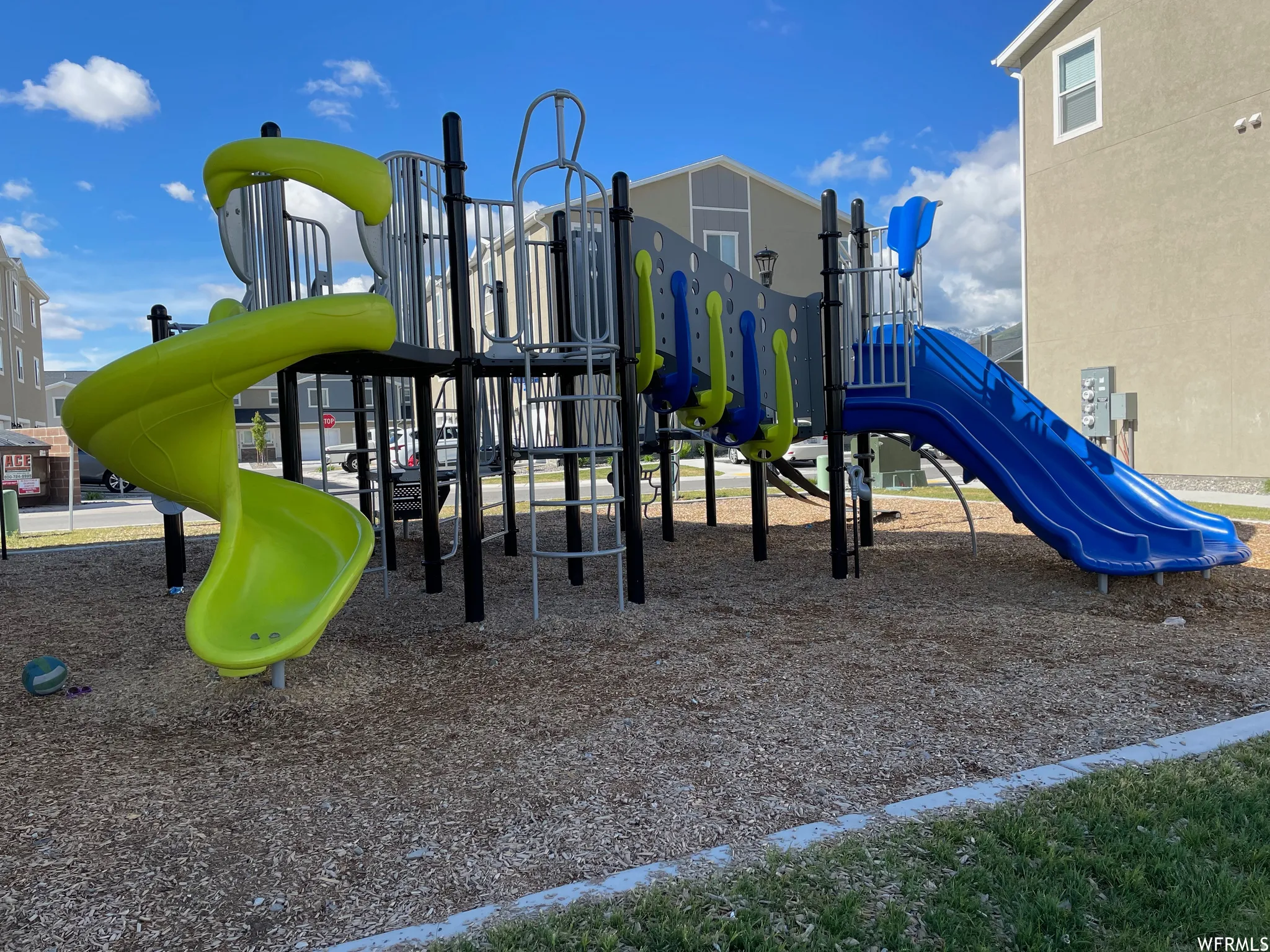Community playground featuring multi-level play structures, two slides, climbing elements, and a wood chip surface