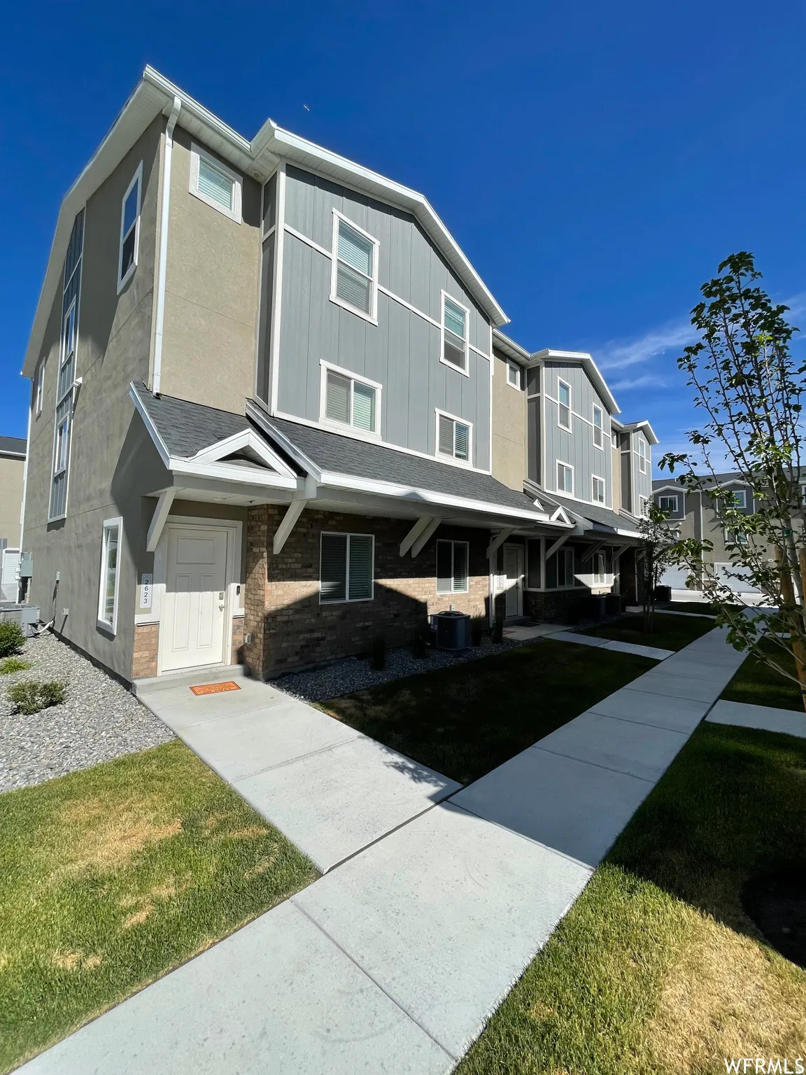 Contemporary townhome exterior featuring light gray vertical siding and tan stucco